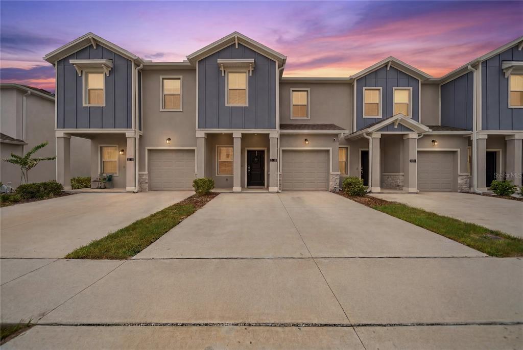 A row of three-story townhomes with blue and beige siding, garages, and concrete driveways — 3161 LAURENT LOOP, DAVENPORT, FL