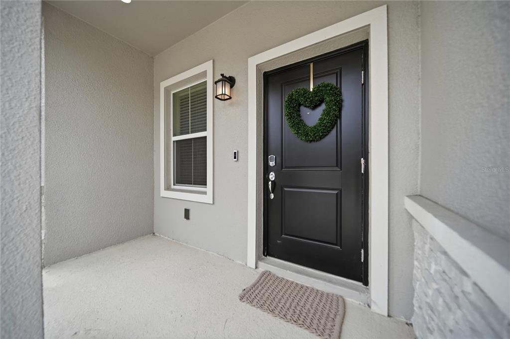 A covered porch features a black front door with a heart-shaped wreath and a window — 3161 LAURENT LOOP, DAVENPORT, FL