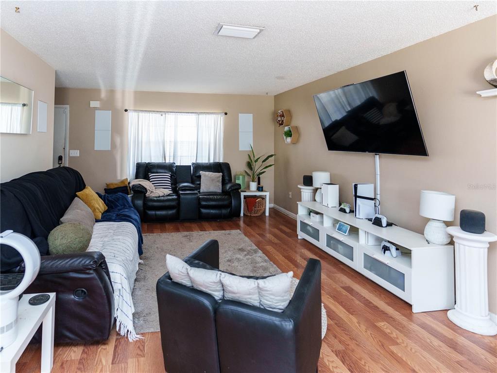 A living room features a wall-mounted television, white media console, and dark leather furniture — 5392 MARINER BOULEVARD, SPRING HILL, FL