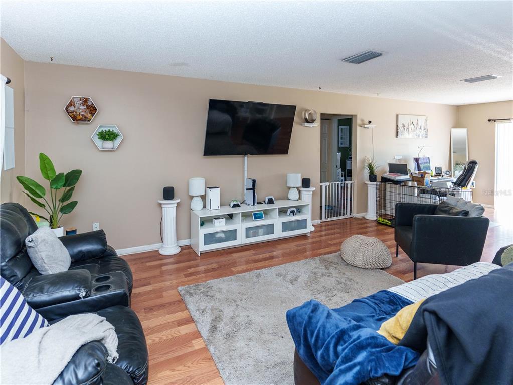 A living room features a wall-mounted television, a white media console, and wood flooring — 5392 MARINER BOULEVARD, SPRING HILL, FL