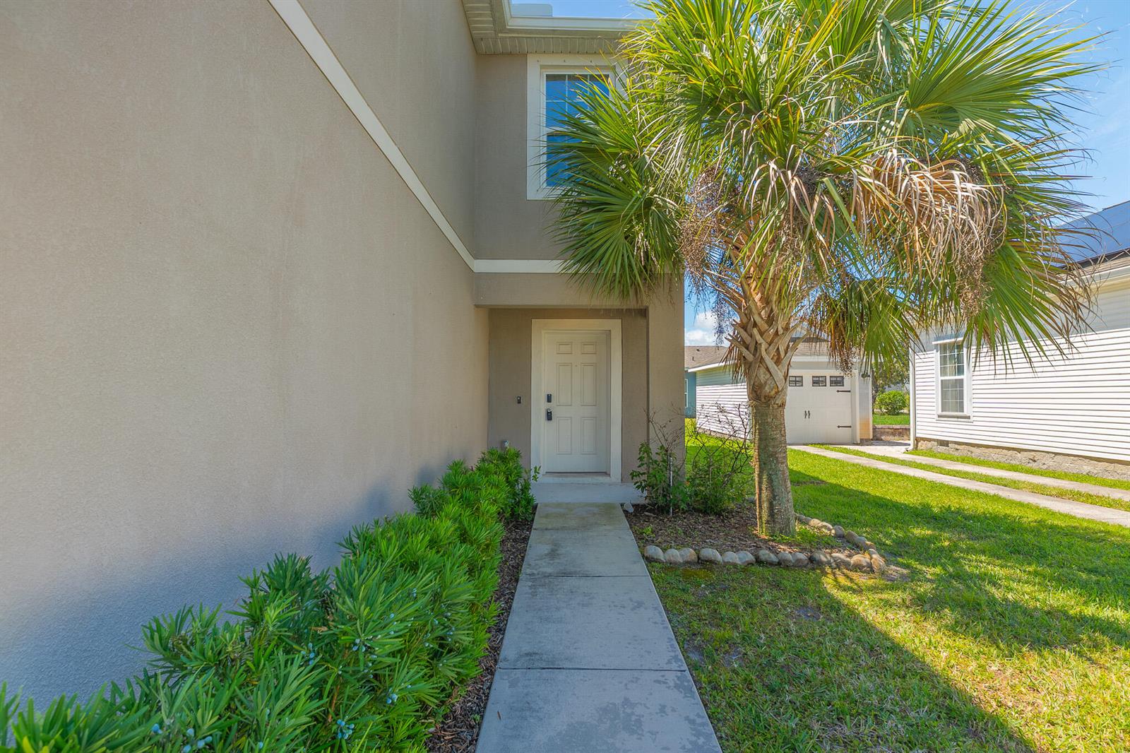 A concrete walkway leads to the front entrance of a beige house with a palm tree — 3351 Liberty Square Way, Fort Pierce FL 34982, FORT PIERCE, FL