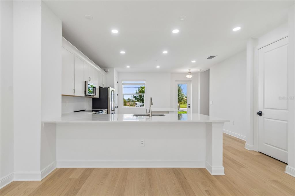 A modern kitchen features white cabinetry, a quartz island with a sink, and light wood flooring — 17806 BROADLEAF LOOP, VENICE, FL