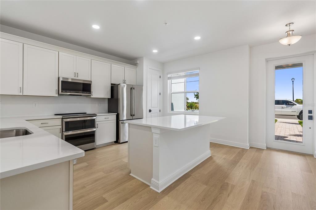 A modern kitchen features white cabinetry, quartz countertops, stainless steel appliances, and light wood flooring — 17806 BROADLEAF LOOP, VENICE, FL