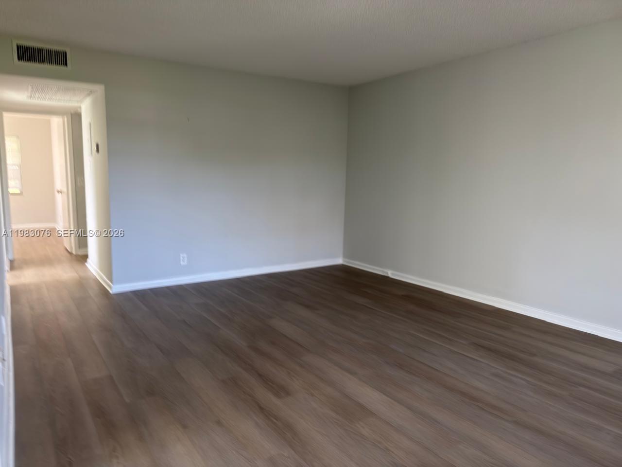 An empty room features light gray walls, dark wood-look flooring, and a white baseboard — 257 Fanshaw G # 257, Boca Raton FL 33434, BOCA RATON, FL