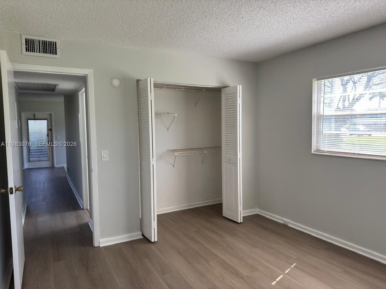 A bedroom with light gray walls, wood-look flooring, an open closet, and a window — 257 Fanshaw G # 257, Boca Raton FL 33434, BOCA RATON, FL