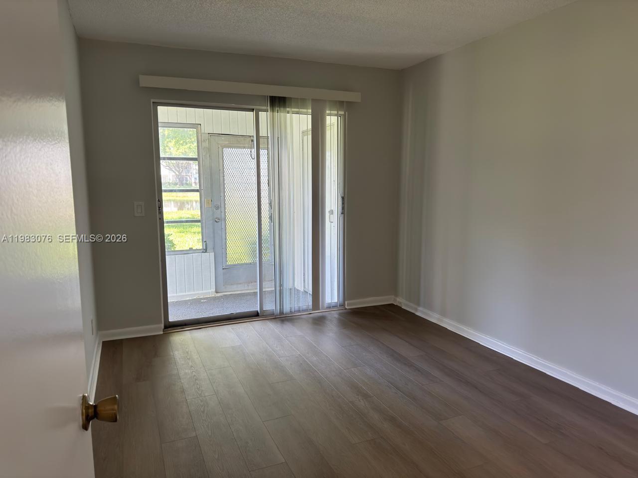 An empty room with wood-look flooring and a sliding glass door leading to a patio — 257 Fanshaw G # 257, Boca Raton FL 33434, BOCA RATON, FL