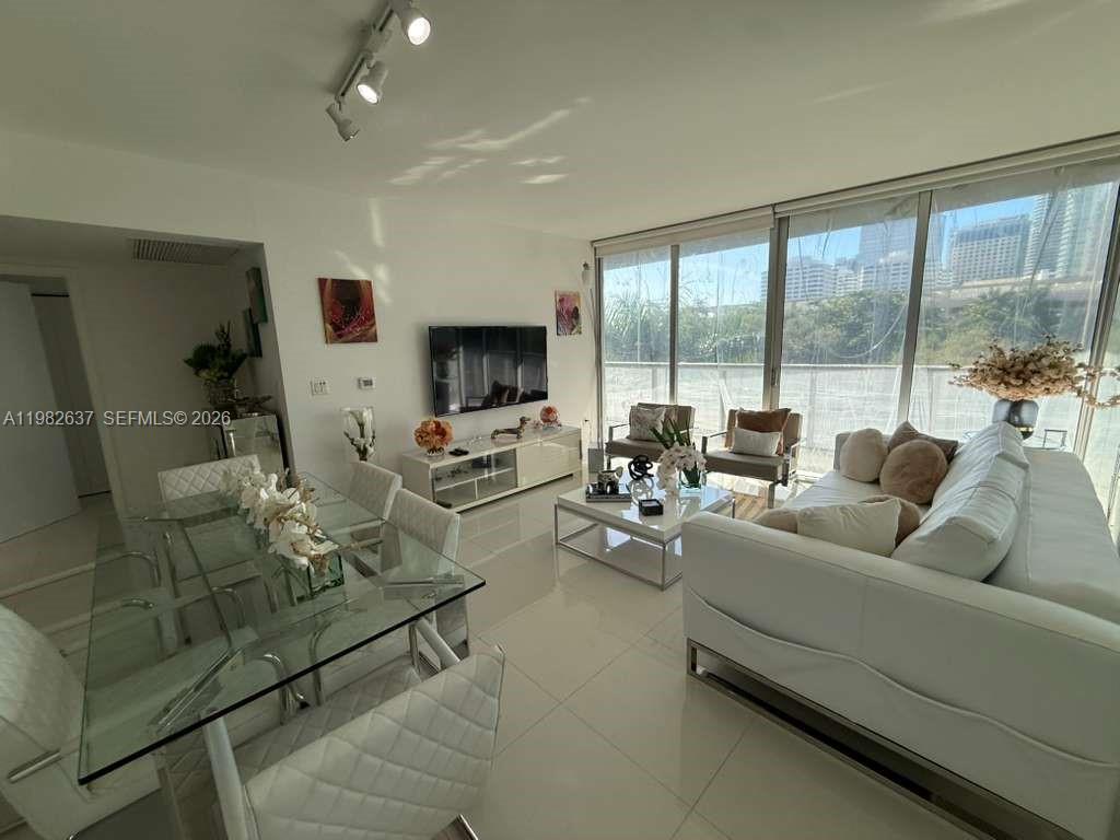 A bright living and dining area features white furniture, tile floors, and floor-to-ceiling windows — 495 Brickell Ave # 511, Miami FL 33131, MIAMI, FL