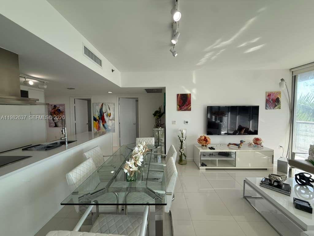 A modern dining and living area features a glass table, white tile floors, and track lighting — 495 Brickell Ave # 511, Miami FL 33131, MIAMI, FL