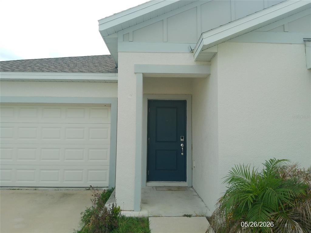 A view of a house exterior featuring a garage, a blue front door, and landscaping — 437 SINGING SANDS CIRCLE, LAKE WALES, FL
