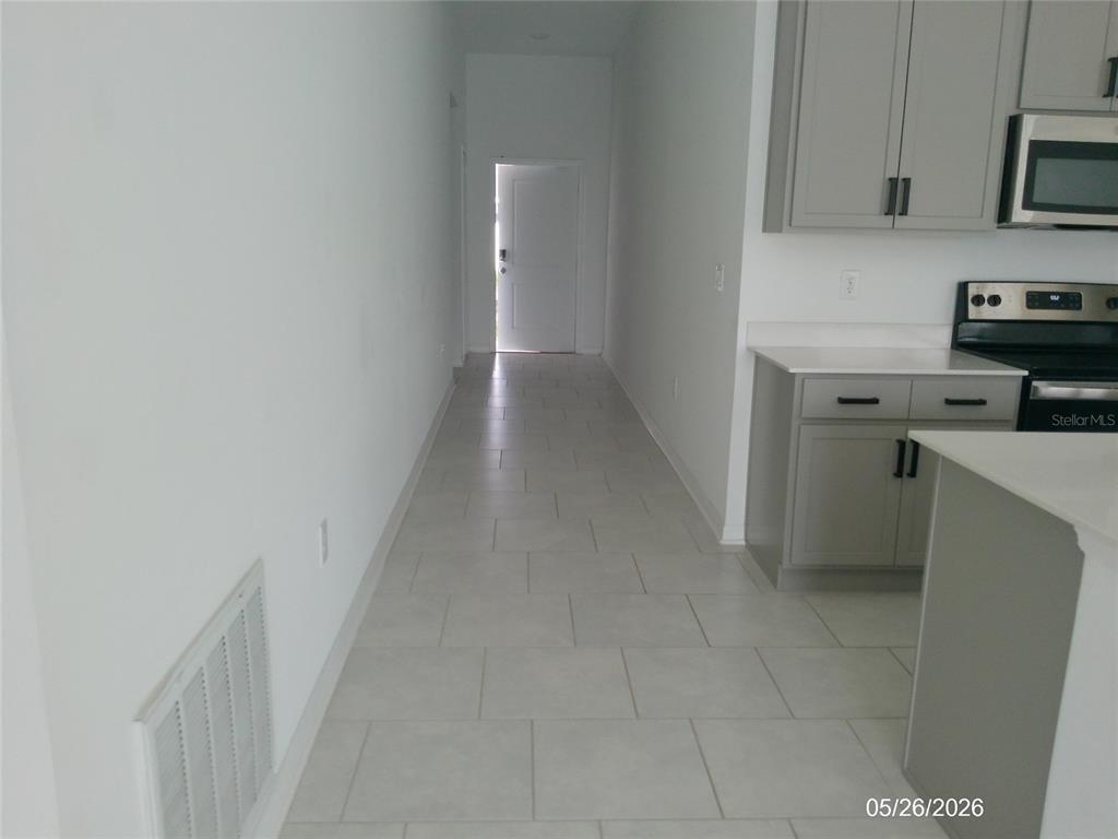 A hallway with light tile flooring leads to an exterior door next to a kitchen — 437 SINGING SANDS CIRCLE, LAKE WALES, FL