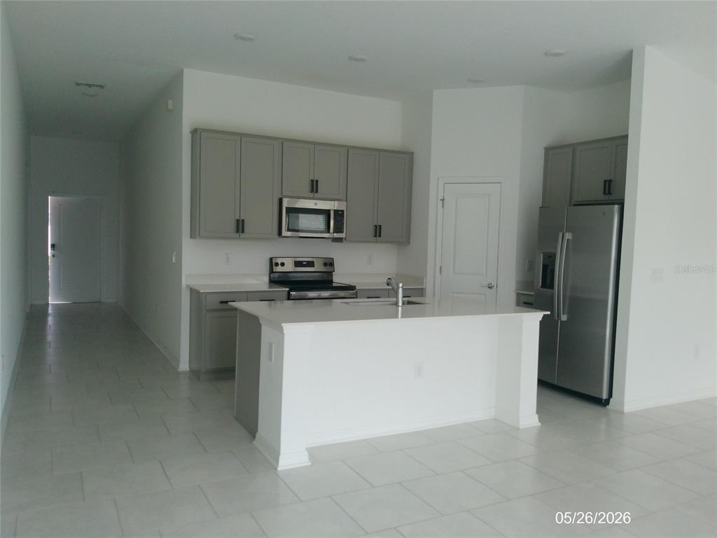 A kitchen features gray cabinets, stainless steel appliances, a white island, and light tile flooring — 437 SINGING SANDS CIRCLE, LAKE WALES, FL