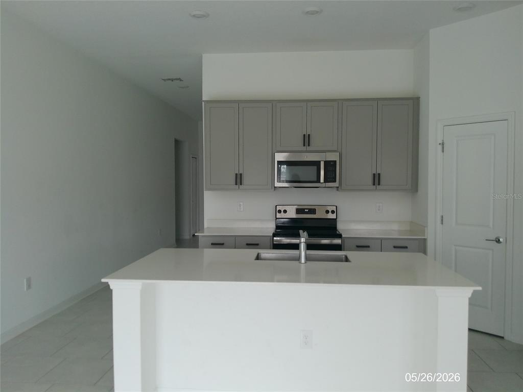 A kitchen features gray cabinets, stainless steel appliances, and a white island with a sink — 437 SINGING SANDS CIRCLE, LAKE WALES, FL