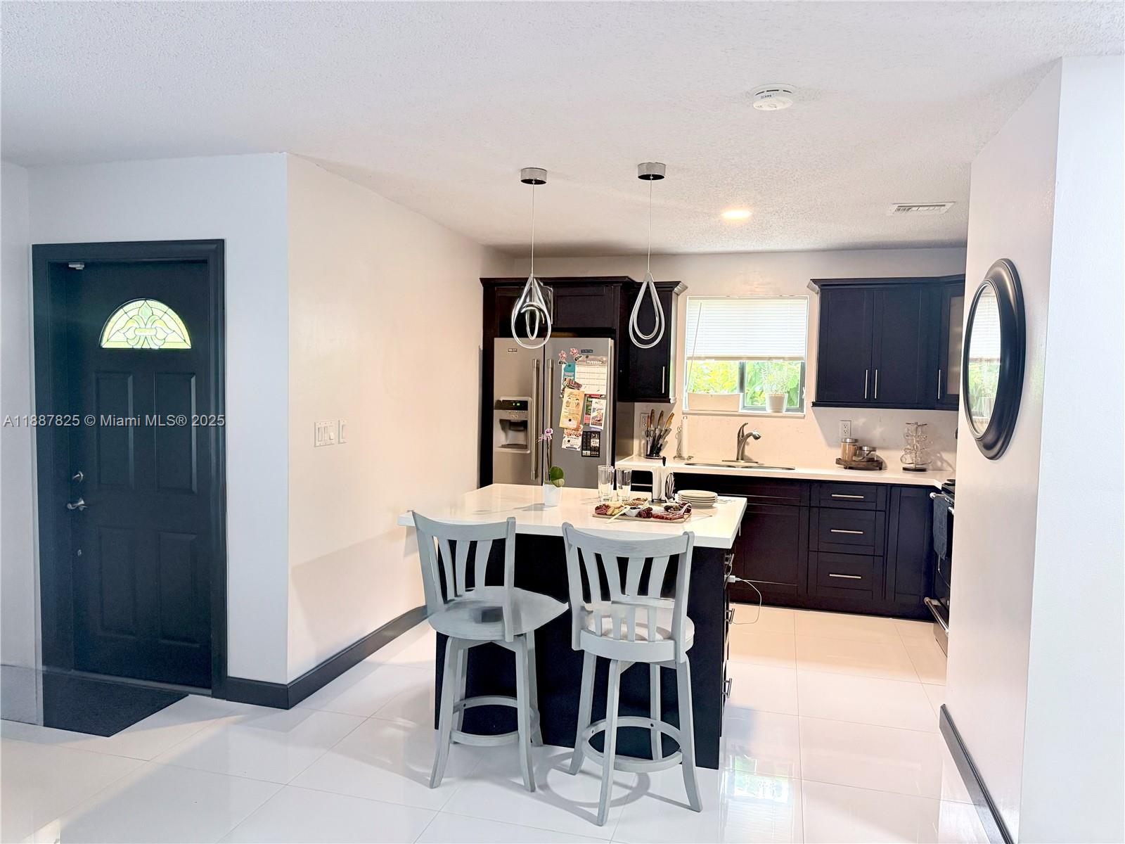 A kitchen features dark cabinets, a white island with two chairs, and white tile floors — 2150 NW 43rd St, Miami FL 33142, MIAMI, FL