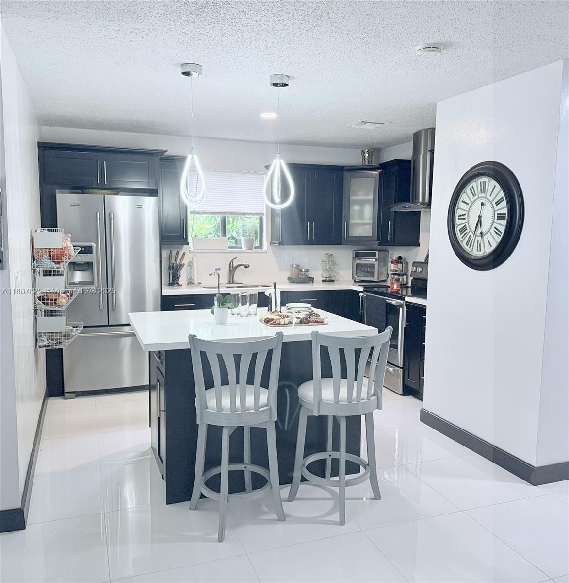 A modern kitchen features dark cabinetry, a white island with two chairs, and stainless appliances — 2150 NW 43rd St, Miami FL 33142, MIAMI, FL