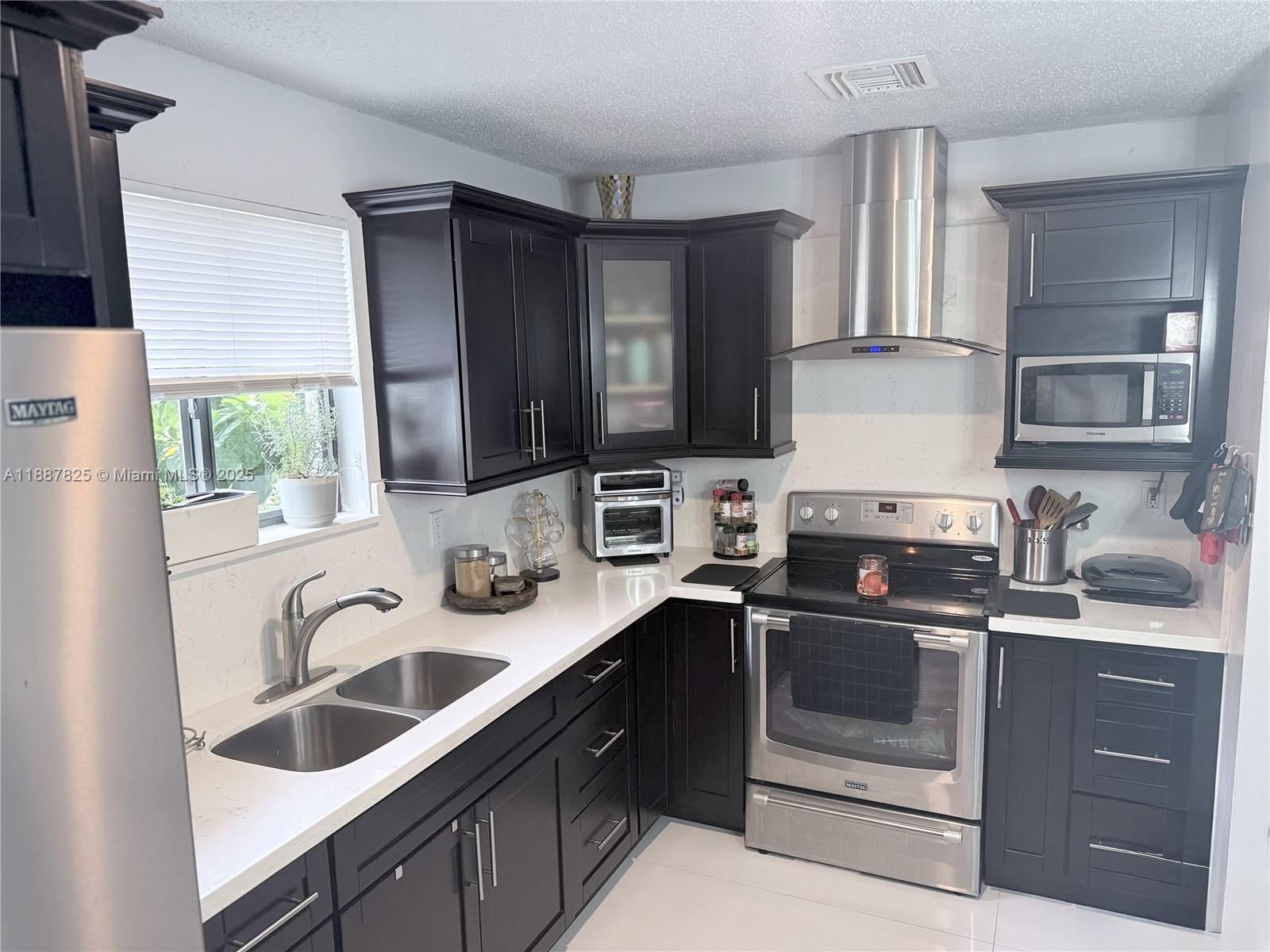 A kitchen features dark cabinetry, stainless steel appliances, white countertops, and a double-basin sink — 2150 NW 43rd St, Miami FL 33142, MIAMI, FL