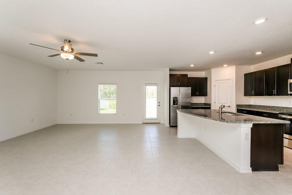 An open-concept kitchen with dark cabinets and granite countertops overlooks a large tiled living area — 1993 SKYBROOKE BOULEVARD, LUTZ, FL