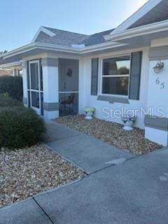 The exterior of a white house features a screened entryway, a window with shutters, and gravel landscaping — 65 ALLWORTHY STREET, PORT CHARLOTTE, FL