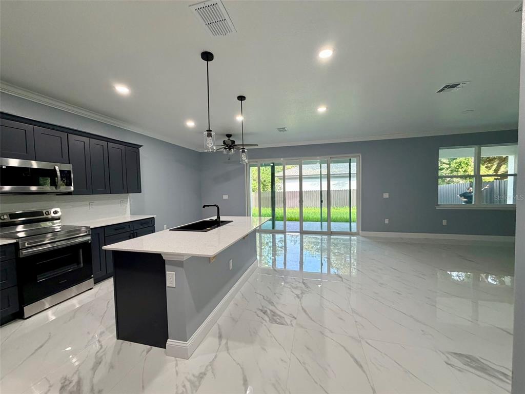 A modern kitchen features dark cabinets, a white quartz island, and marble-look tile flooring — 1450 IRMA ROAD, EUSTIS, FL