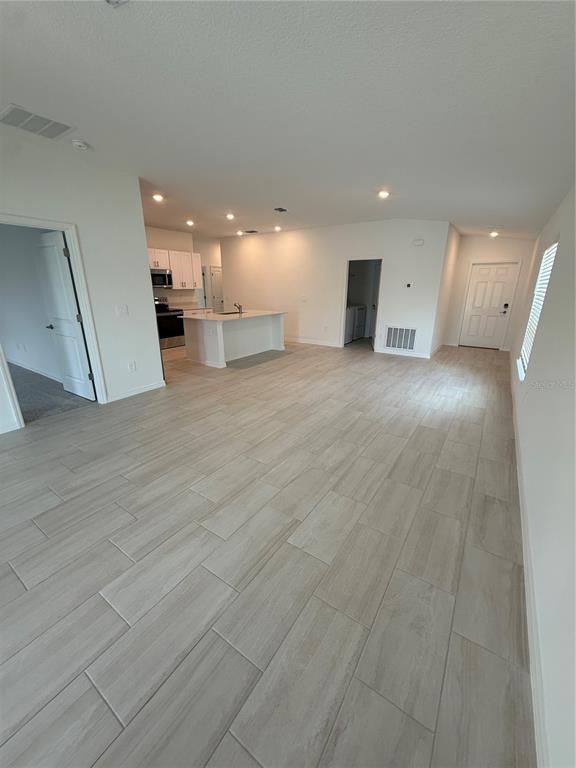 An open-concept living area features light-colored tile flooring, a kitchen island, and recessed lighting — 32985 TWIN FLOWER AVE, WESLEY CHAPEL, FL