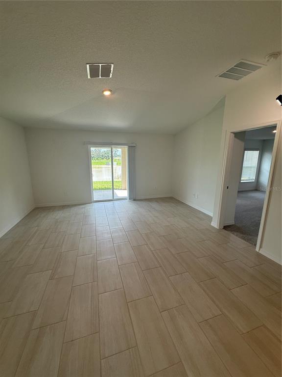 An open living area features light-colored tile flooring, a vaulted ceiling, and sliding glass doors — 32985 TWIN FLOWER AVE, WESLEY CHAPEL, FL