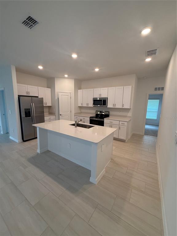 A modern kitchen features white cabinets, stainless steel appliances, and a central island with quartz countertops — 32985 TWIN FLOWER AVE, WESLEY CHAPEL, FL