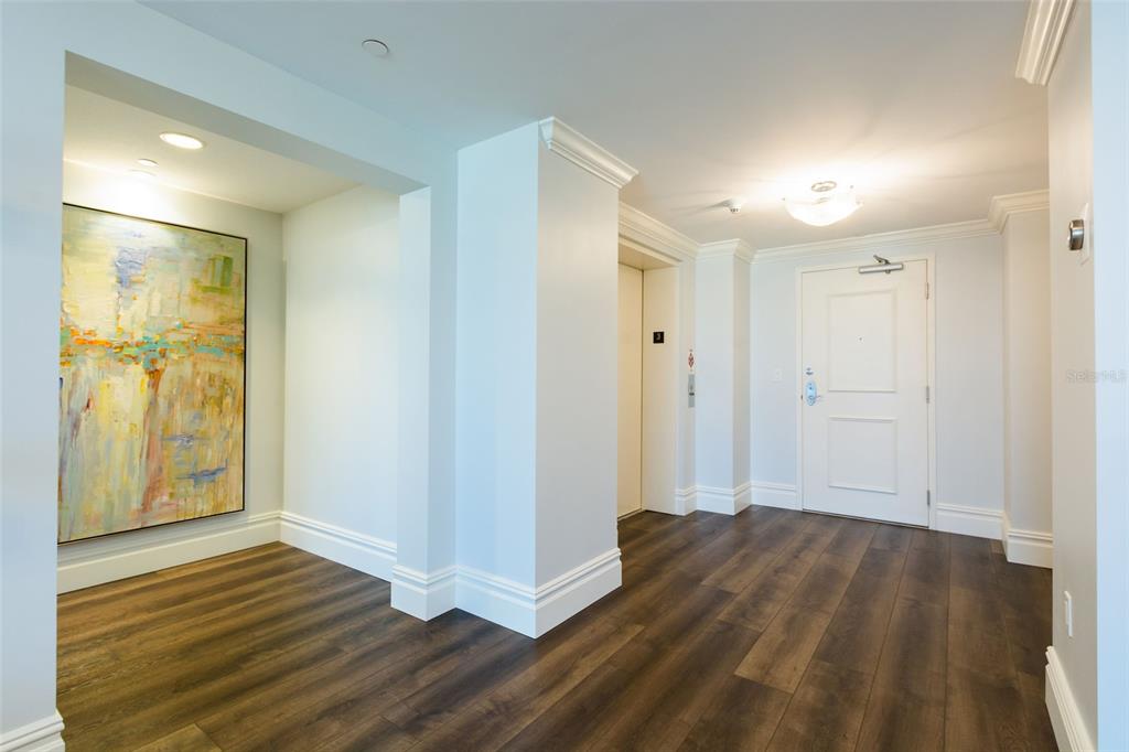 A bright foyer features dark wood flooring, white trim, a modern light fixture, and abstract art — 301 S GULFVIEW BOULEVARD UNIT 304, CLEARWATER BEACH, FL