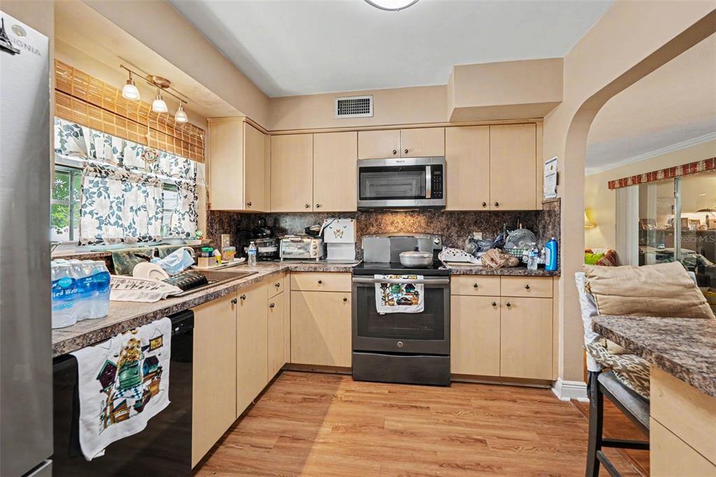 A kitchen with light wood cabinets, dark countertops, stainless steel appliances, and wood-look flooring — 8948 108TH STREET N, SEMINOLE, FL