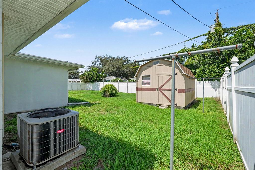 A grassy backyard features a white vinyl fence, a small storage shed, and mature trees — 8948 108TH STREET N, SEMINOLE, FL