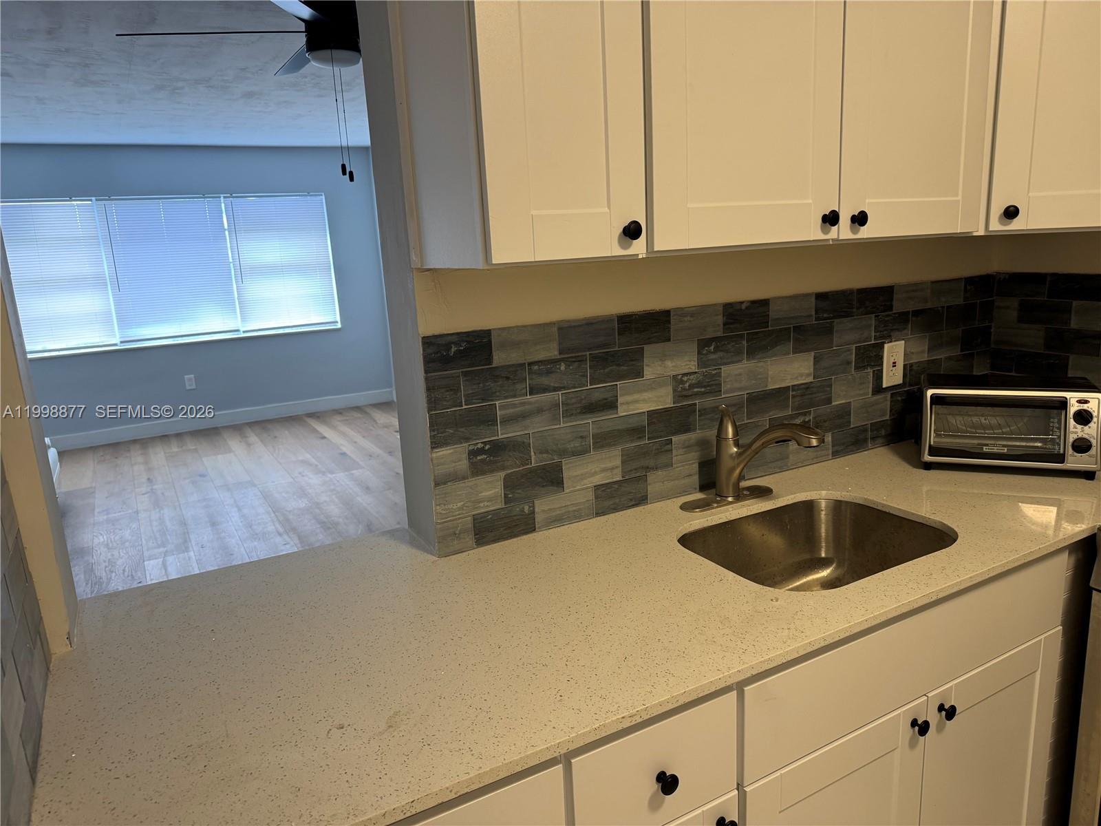 A kitchen features white cabinets, a speckled countertop, and a gray tiled backsplash — 6720 Arbor Dr # 207, Miramar FL 33023, MIRAMAR, FL