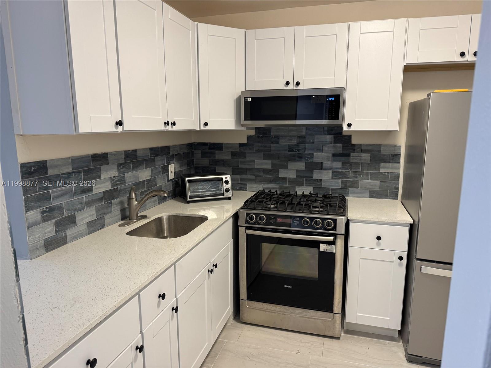 A kitchen features white cabinetry, stainless steel appliances, quartz countertops, and a blue tiled backsplash — 6720 Arbor Dr # 207, Miramar FL 33023, MIRAMAR, FL