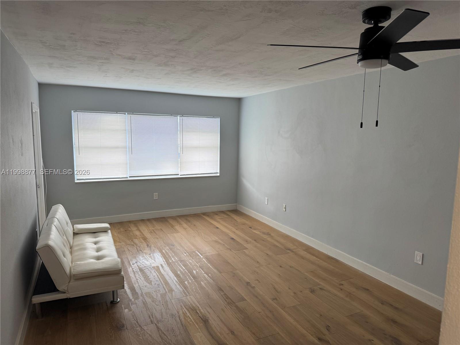 A living room features light wood-look flooring, pale blue walls, a white futon, and a ceiling fan — 6720 Arbor Dr # 207, Miramar FL 33023, MIRAMAR, FL