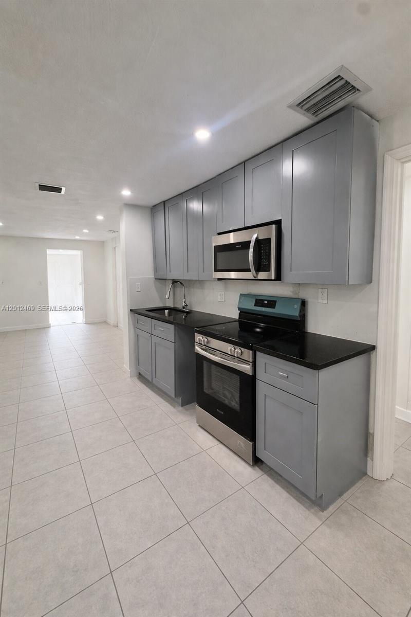A modern kitchen features gray cabinets, black countertops, and stainless steel appliances — 1861 NW 112th St, Miami FL 33167, MIAMI, FL