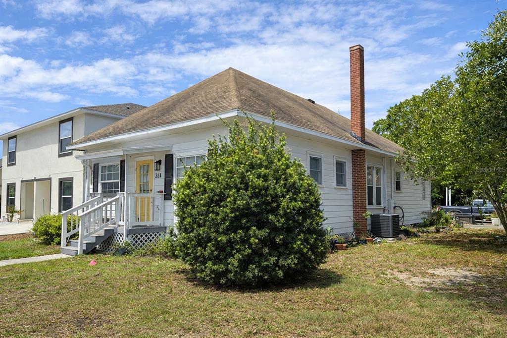 A white single-story house with a yellow front door and a brick chimney — 231 AVENUE A NE, WINTER HAVEN, FL