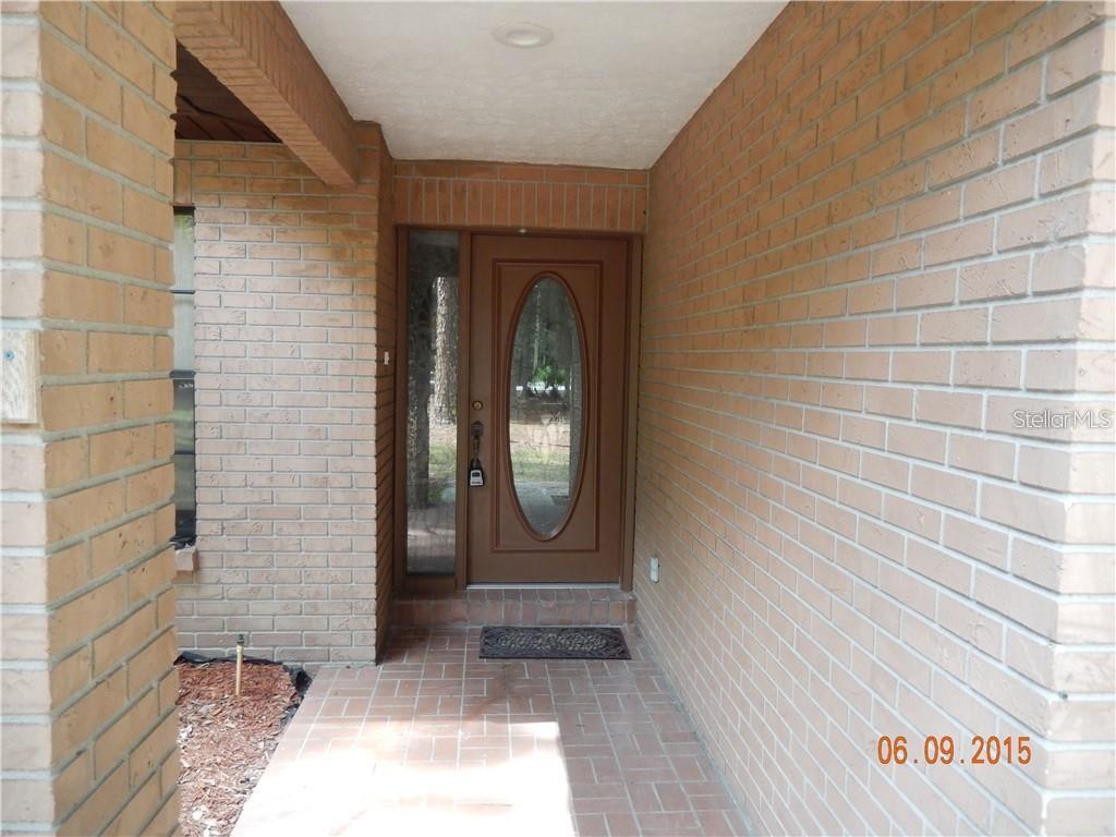 A brick-walled entryway features a brown front door with an oval glass insert — 8925 QUAIL RUN DRIVE, WESLEY CHAPEL, FL
