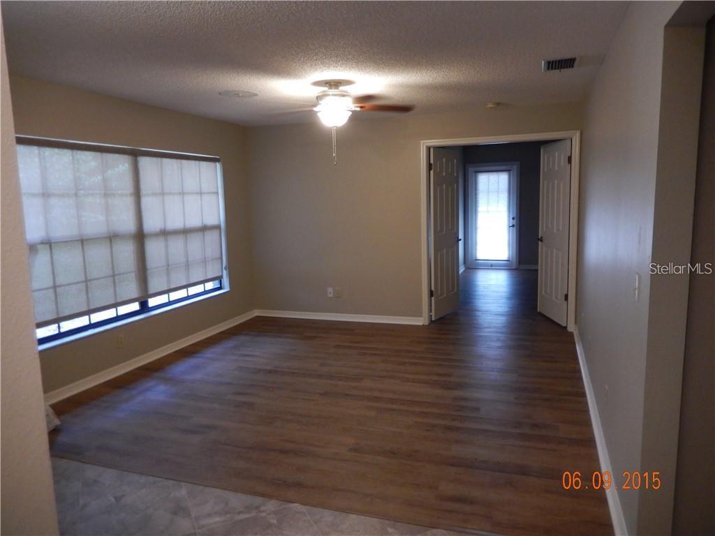 An empty room features wood-look flooring, a ceiling fan, and double doors leading outside — 8925 QUAIL RUN DRIVE, WESLEY CHAPEL, FL