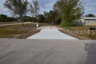 A concrete driveway apron leads from a paved road onto a vacant, grassy residential lot — 27494 BANDIT DRIVE, PUNTA GORDA, FL