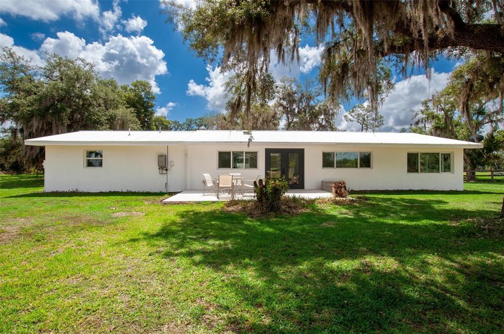 A white single-story house with a metal roof sits on a grassy lawn under trees — 1635 SW RODGERS AVENUE, ARCADIA, FL