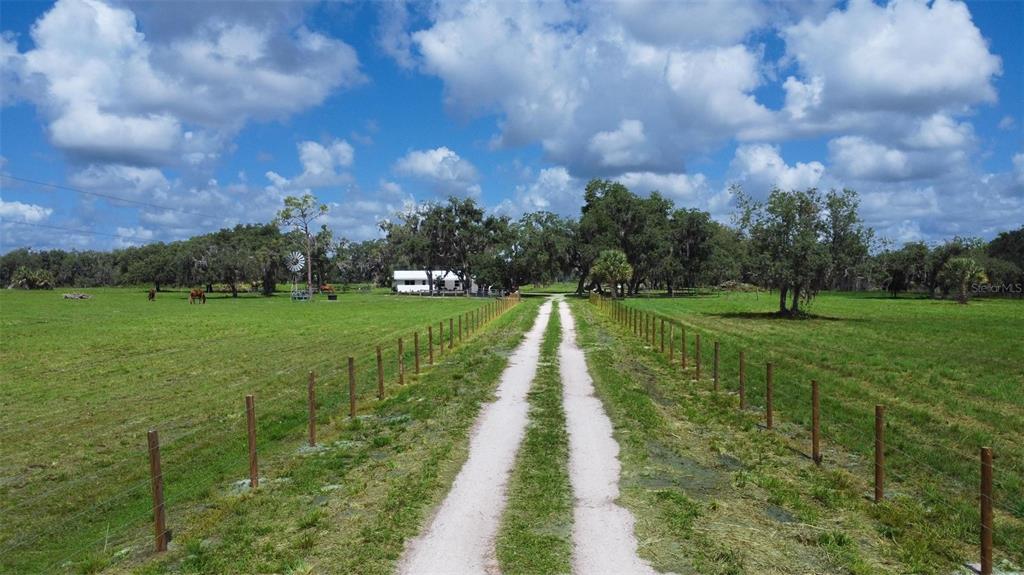 A dirt driveway leads through a grassy pasture toward a white house with a windmill — 1635 SW RODGERS AVENUE, ARCADIA, FL