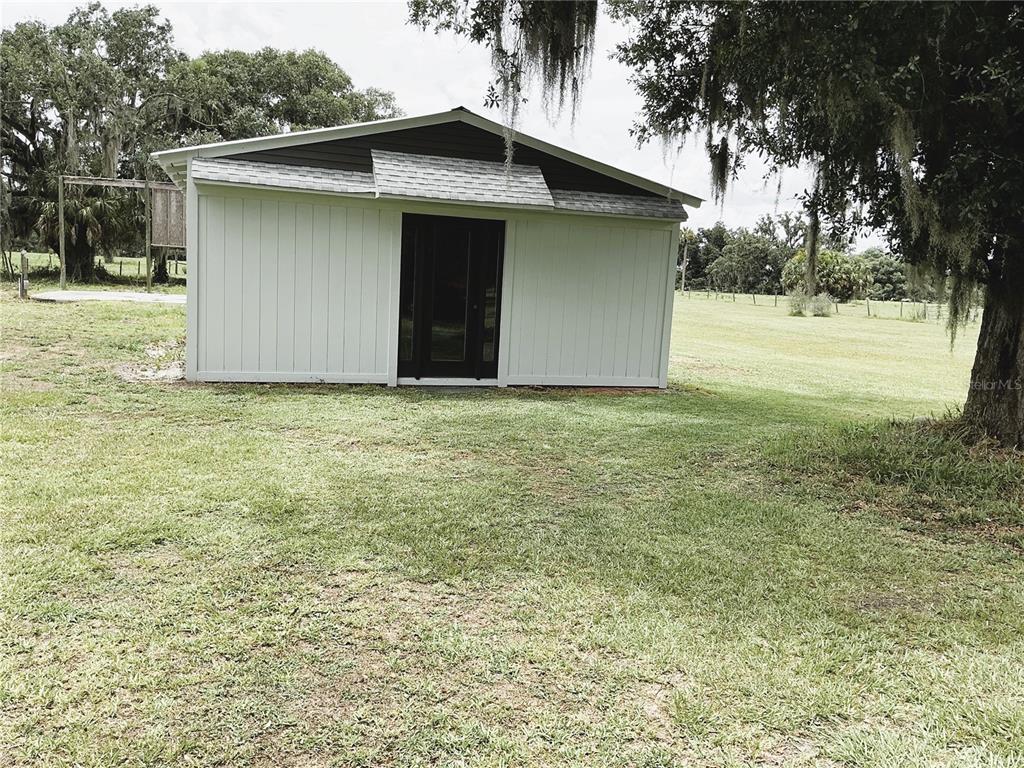 A white shed with a dark door and a small roof overhang stands on grass — 1635 SW RODGERS AVENUE, ARCADIA, FL