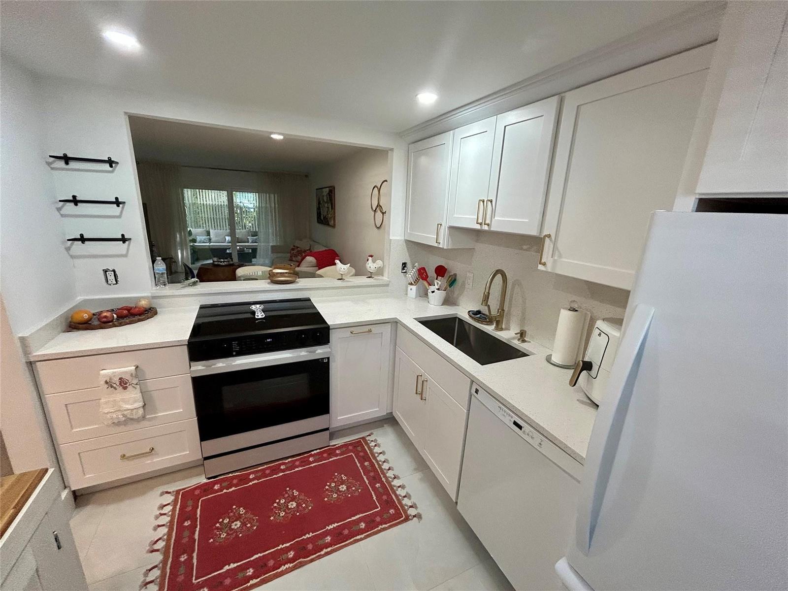 A white kitchen features a stove, sink, dishwasher, and a pass-through window to the living area — 3060 Holiday Springs Boulevard # 102, Margate FL 33063, MARGATE, FL