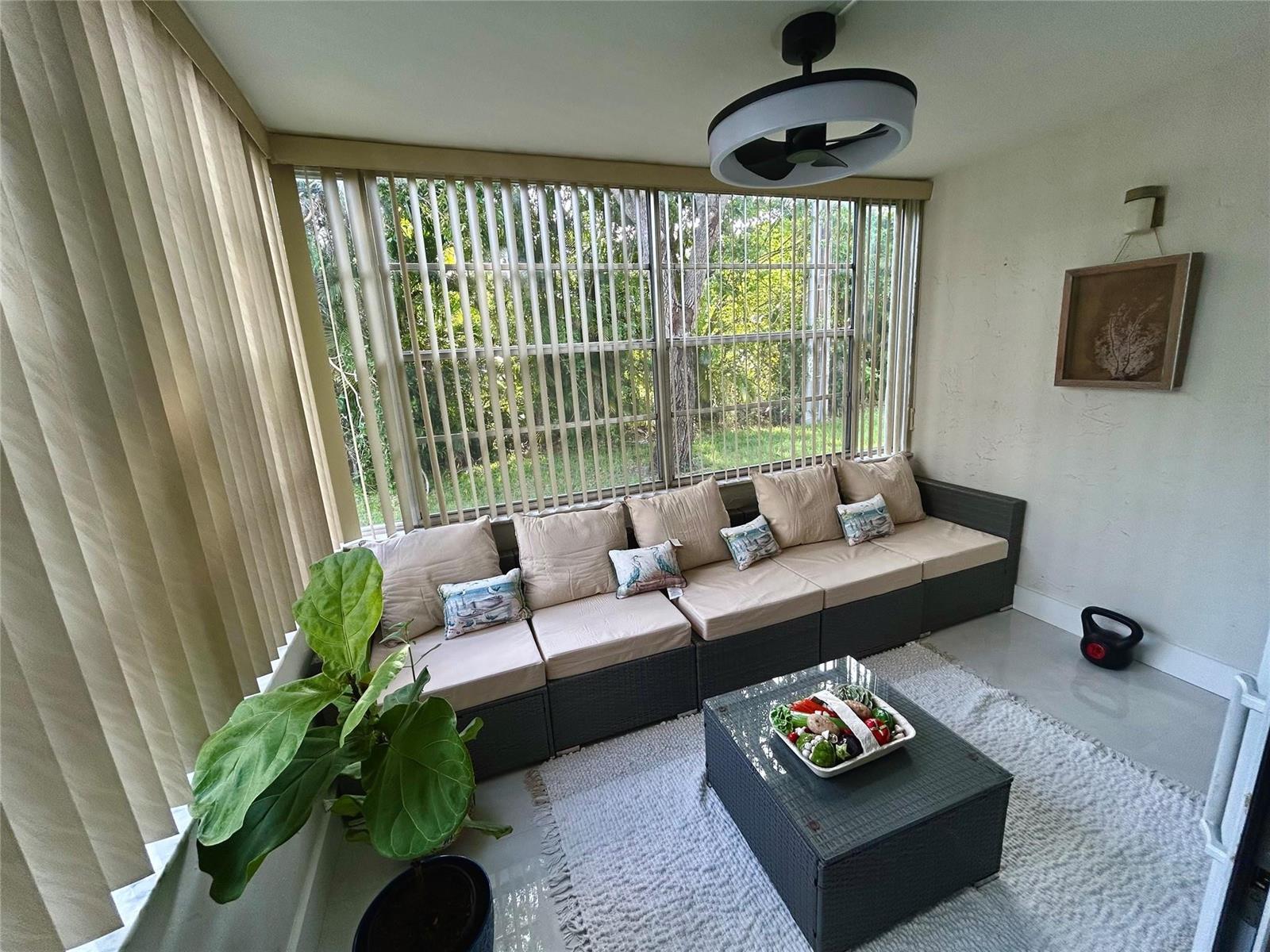 A sunroom features a modular wicker sofa, a glass-topped coffee table, and vertical window blinds — 3060 Holiday Springs Boulevard # 102, Margate FL 33063, MARGATE, FL