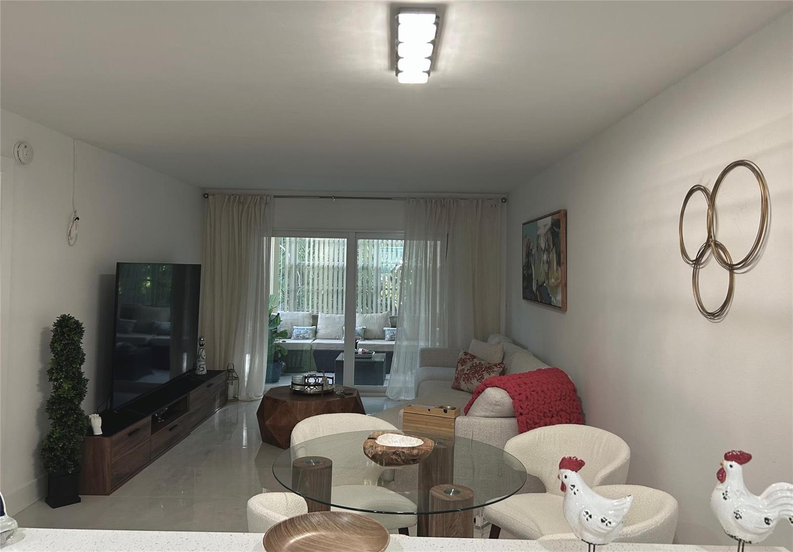 A living and dining area features a glass table, white chairs, and a sliding door — 3060 Holiday Springs Boulevard # 102, Margate FL 33063, MARGATE, FL