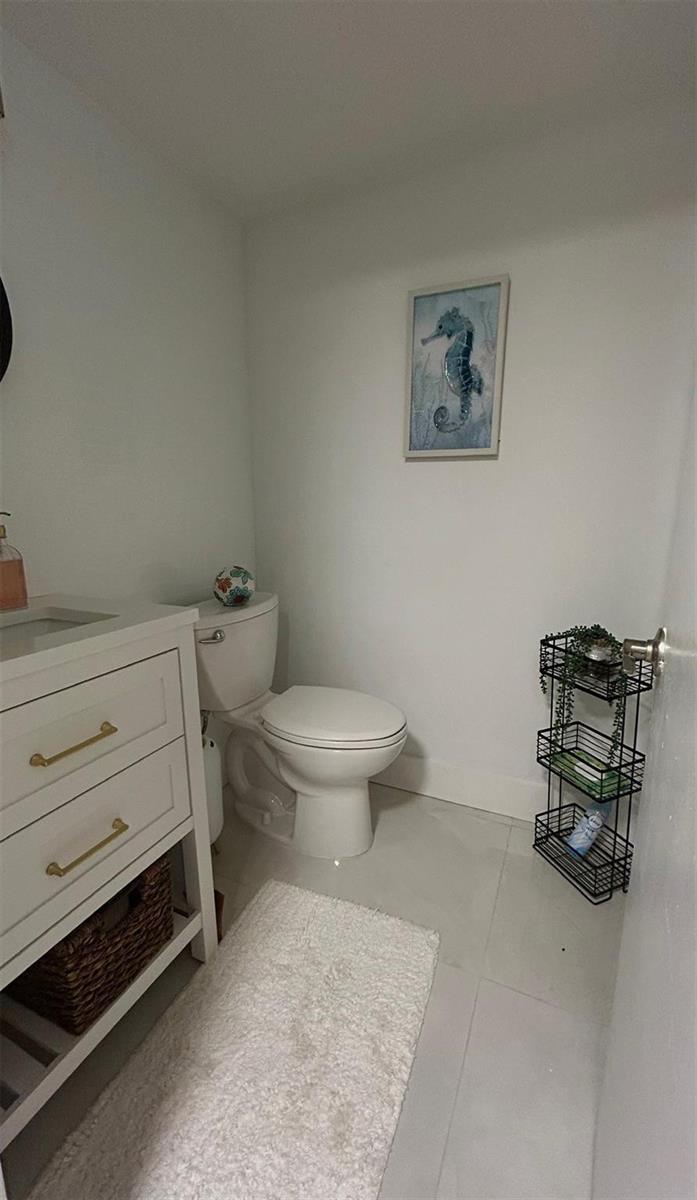 A small bathroom features a white vanity, a toilet, and a three-tiered wire storage rack — 3060 Holiday Springs Boulevard # 102, Margate FL 33063, MARGATE, FL
