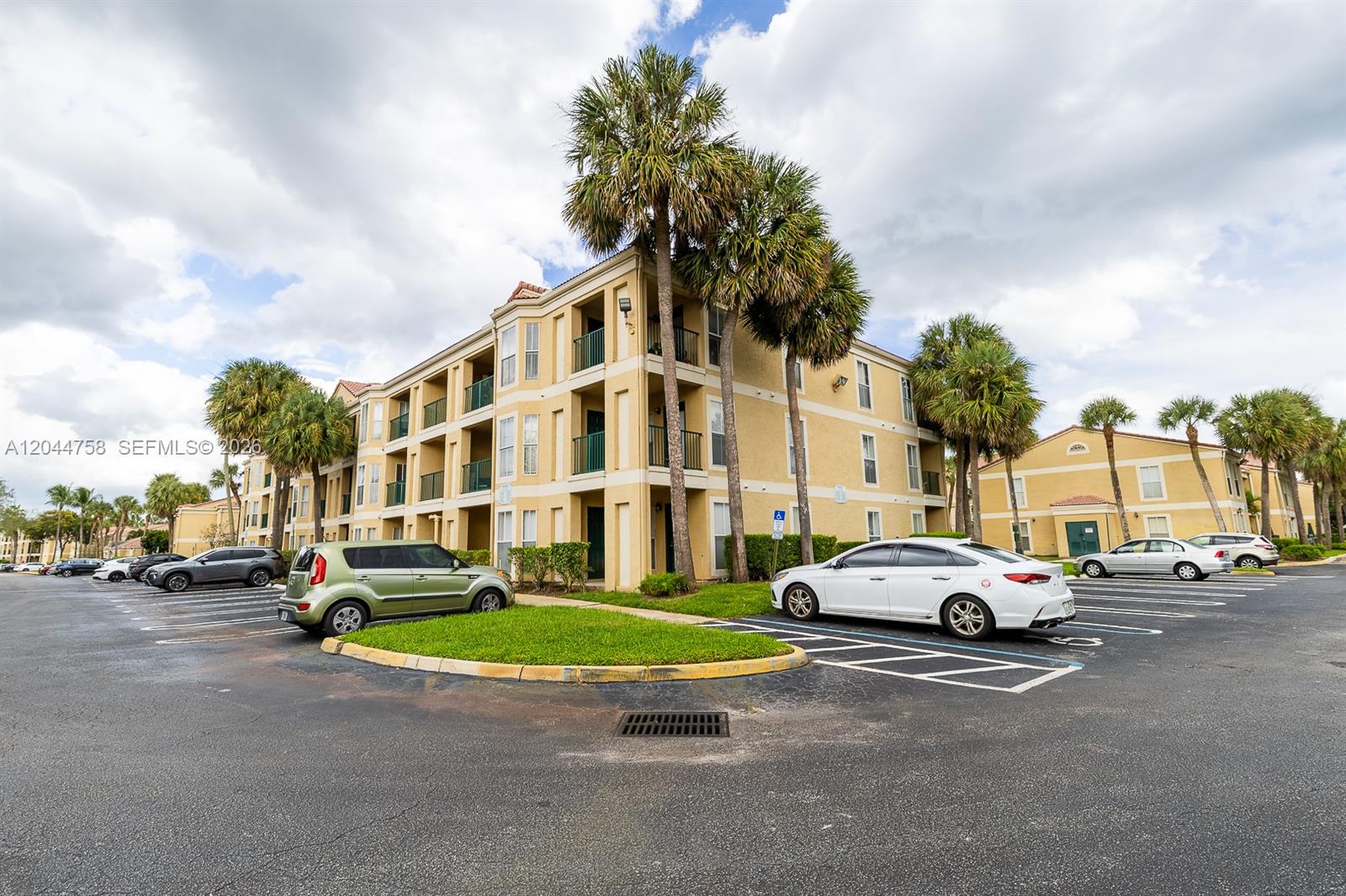A multi-story apartment building with a parking lot and palm trees under a cloudy sky — CORAL SPRINGS, FL