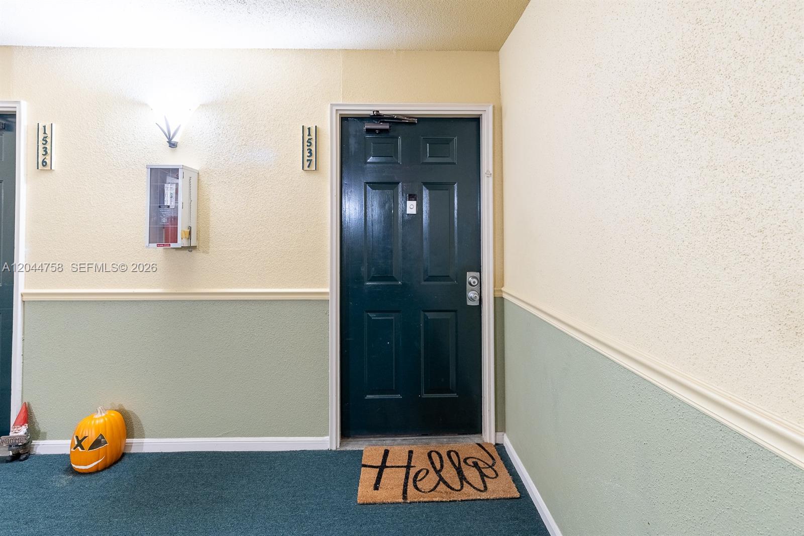 A dark green apartment door with a welcome mat sits between two cream-colored walls — CORAL SPRINGS, FL