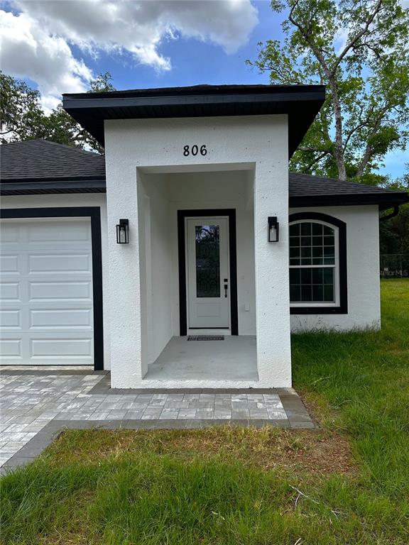 The exterior of a white stucco house features a black-trimmed front door and garage — 806 W LOWRY LANE, TAMPA, FL