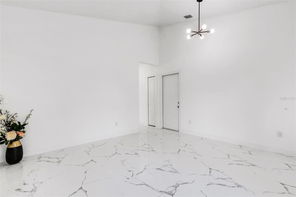 A bright, empty room features white walls, a modern chandelier, and white marble-patterned tile flooring — 806 W LOWRY LANE, TAMPA, FL