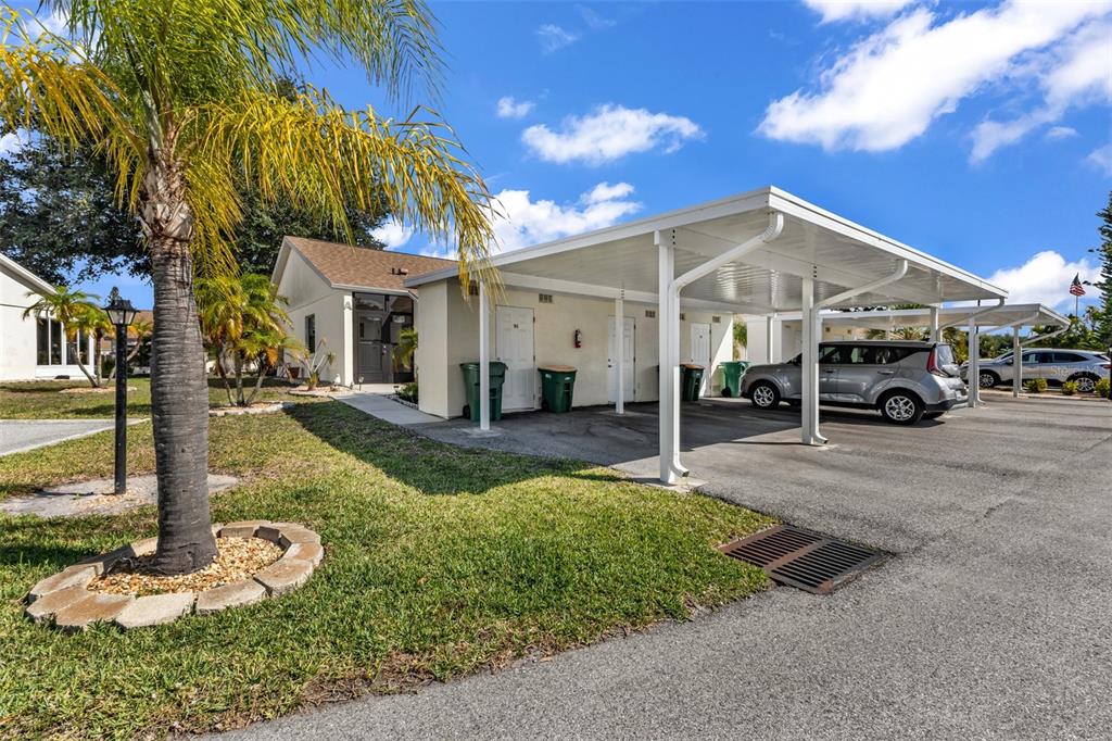 A single-story building with a white carport, green trash bins, and a palm tree — 6796 GASPARILLA PINES BOULEVARD UNIT 105, ENGLEWOOD, FL