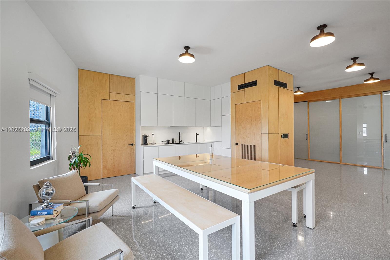 A modern room features a kitchen with white cabinets, wood paneling, and a glass-topped table — 1800 N Miami Ave, Miami FL 33136, MIAMI, FL