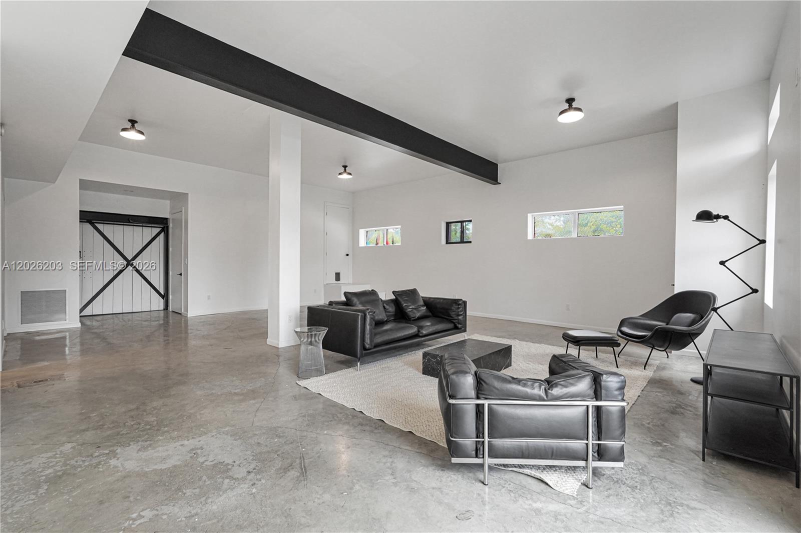 A minimalist living room features a concrete floor, black leather furniture, and an exposed beam — 1800 N Miami Ave, Miami FL 33136, MIAMI, FL
